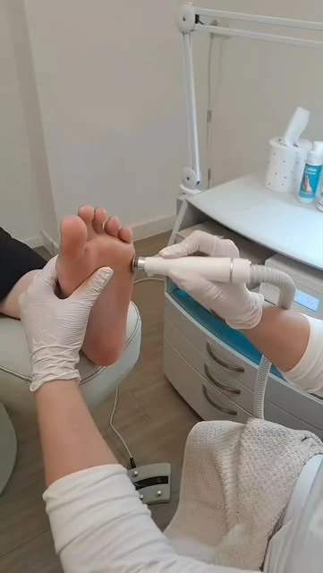 Behandlung im Studio: behandschuhte Hände führen das Pediküregerät an der Fußsohle